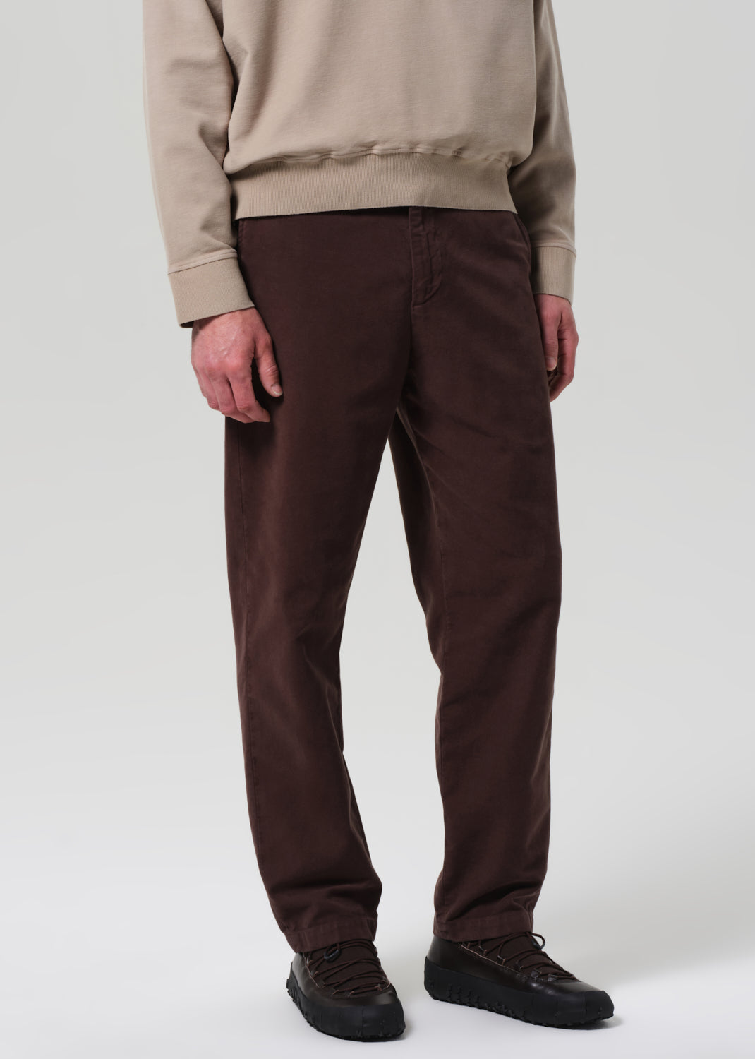 Person wearing brown pants and beige sweatshirt on a plain background
