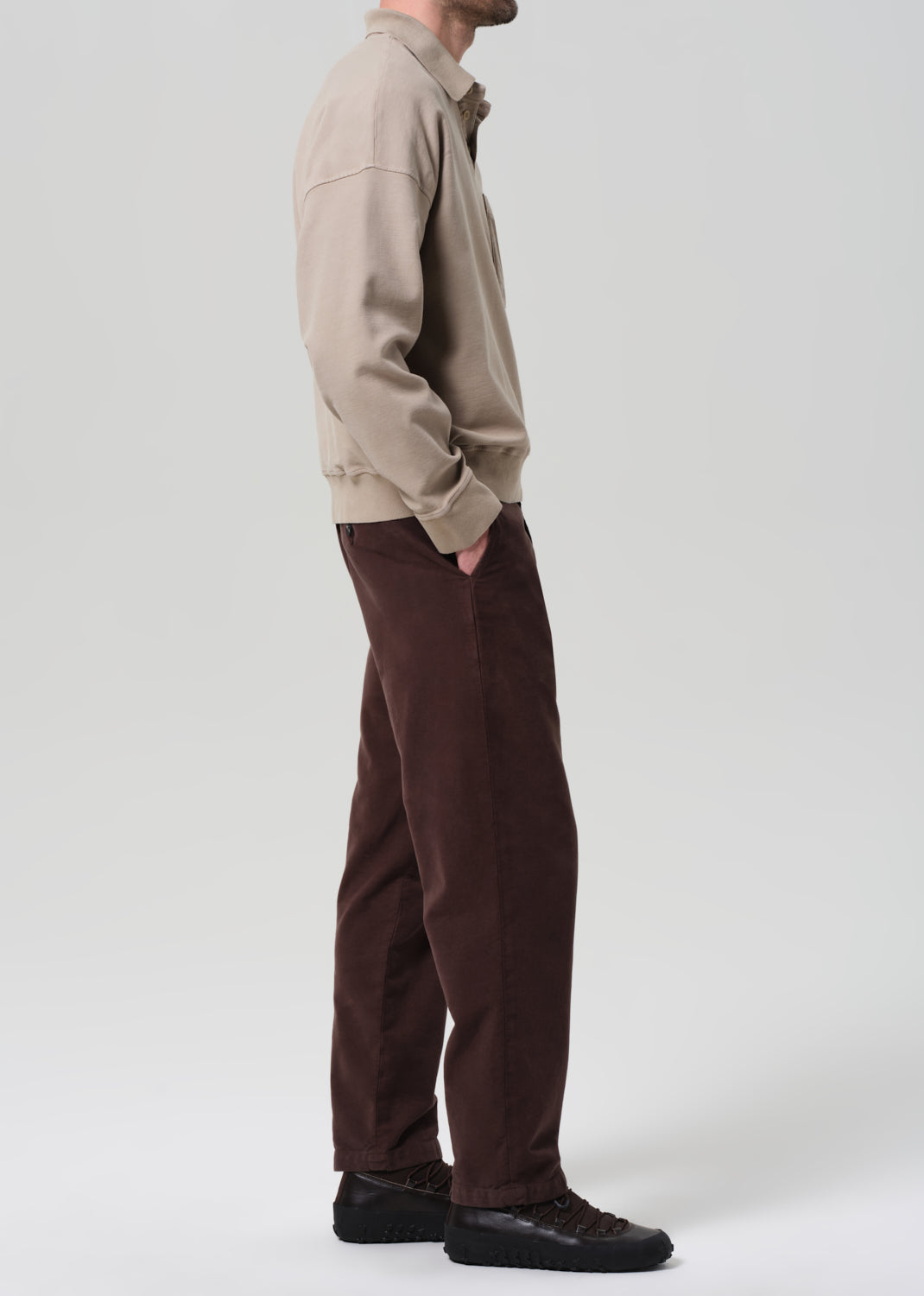 Person wearing a beige jacket and brown pants on a plain background