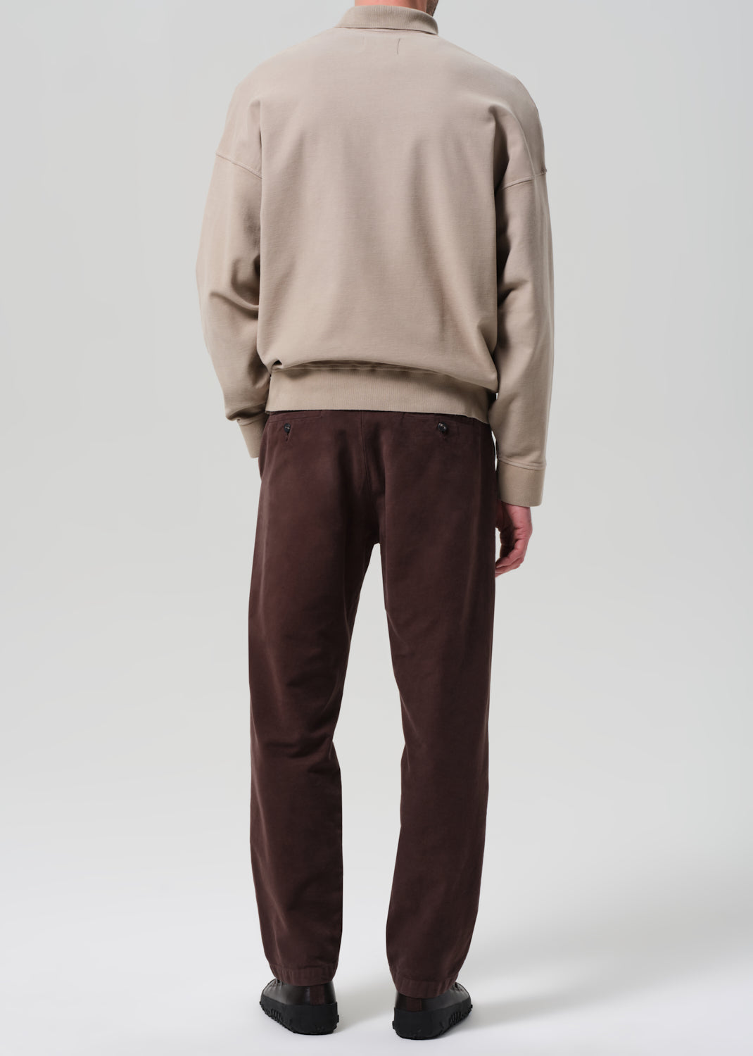 Person wearing a beige sweater and brown pants on a plain background