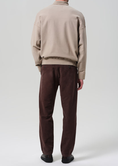 Person wearing a beige sweater and brown pants on a plain background