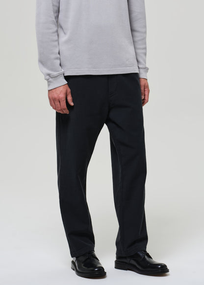 Person wearing a light gray crewneck and charcoal pants on a grey background
