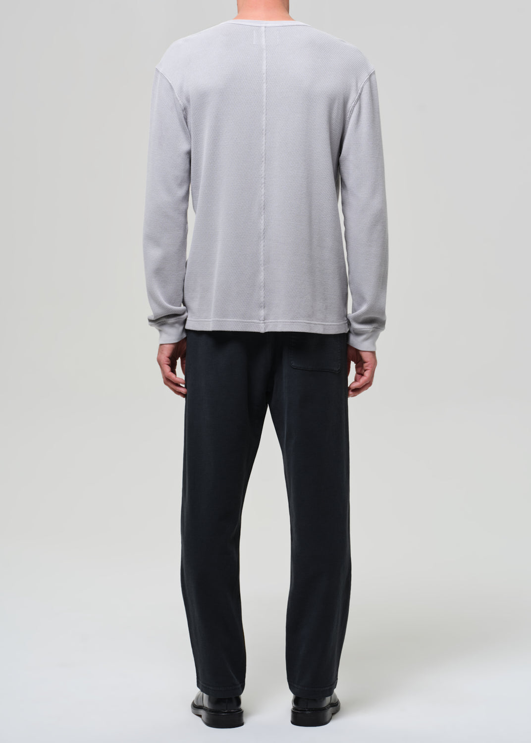 Person wearing a light gray crewneck and charcoal pants on a grey background