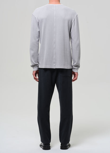 Person wearing a light gray crewneck and charcoal pants on a grey background