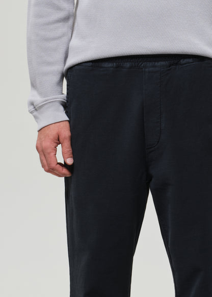 Person wearing a light gray crewneck and charcoal pants on a grey background