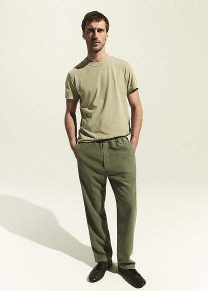 Man wearing a beige t-shirt and green pants on a white background