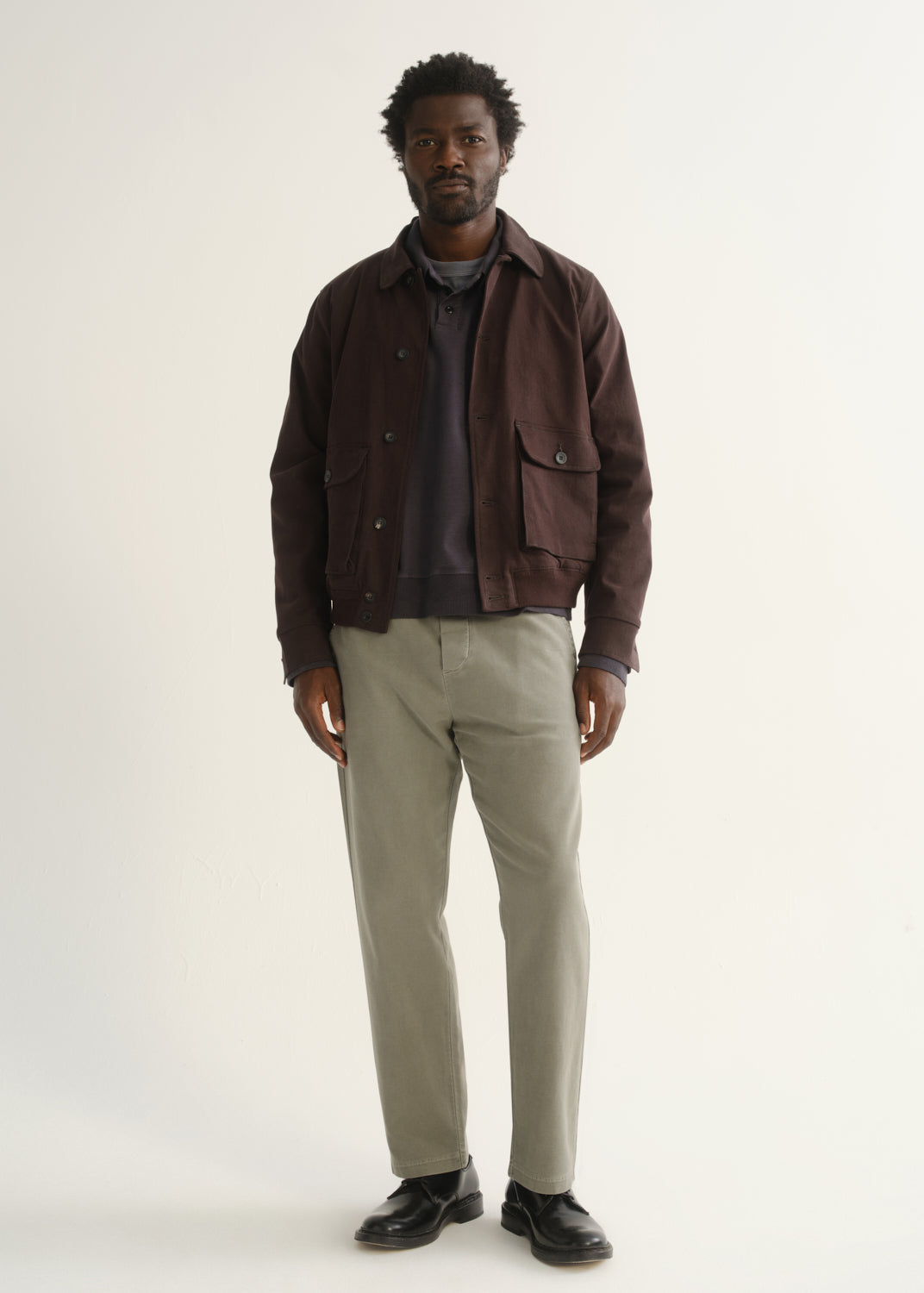 Person wearing light beige straight leg pants with a dark brown jacket, dark shirt, and black shoes, front full body view on a light grey background.