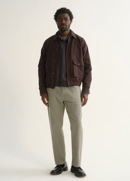 Person wearing light beige straight leg pants with a dark brown jacket, dark shirt, and black shoes, front full body view on a light grey background.