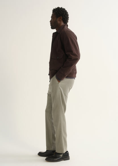 Person wearing light beige straight leg pants with a dark brown jacket and black shoes, side full body view on a light grey background.