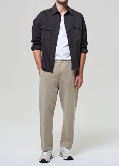 Person wearing a grey shirt, white t-shirt, beige pants, and white sneakers on a plain background