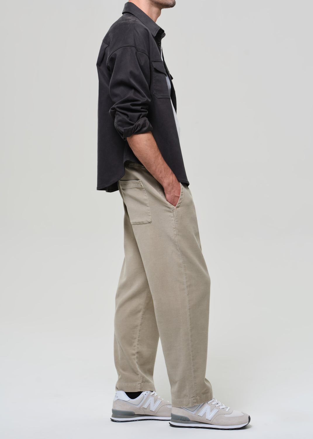 Person wearing a grey shirt, white t-shirt, beige pants, and white sneakers on a plain background