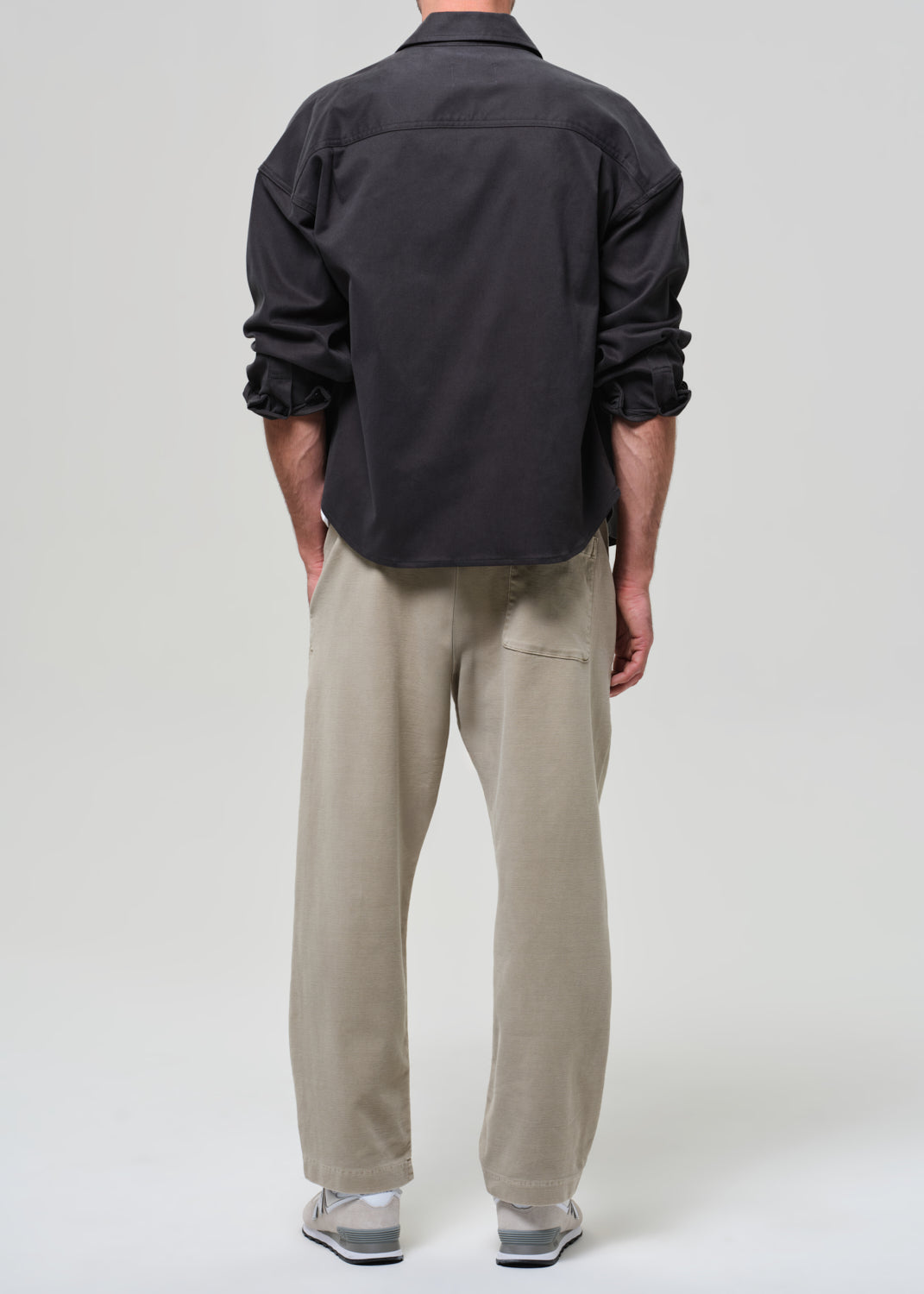 Person wearing a grey shirt, white t-shirt, beige pants, and white sneakers on a plain background