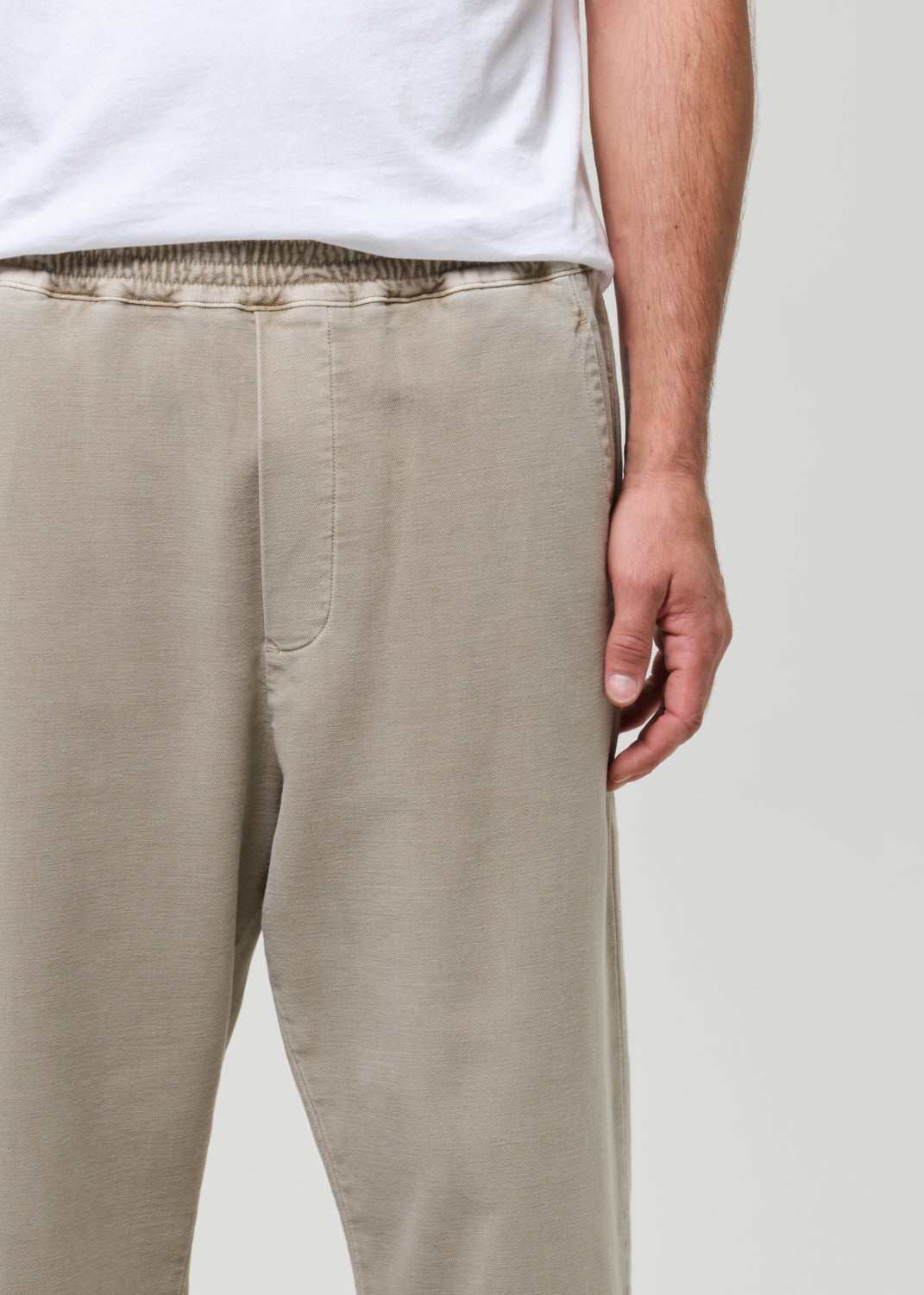 Person wearing beige pants and a white shirt on a plain background