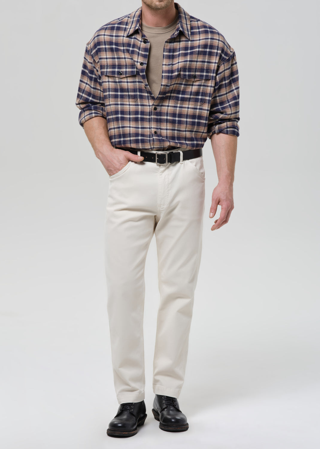 Man wearing a plaid shirt, beige pants, and black shoes on a grey background.