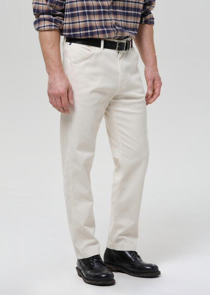 A person wearing off-white straight-leg chinos, a navy and tan plaid shirt, a black belt, and black leather shoes, standing against a grey background.