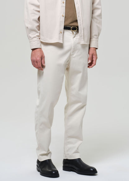 Person wearing a beige jacket, white pants, and black shoes on a plain background