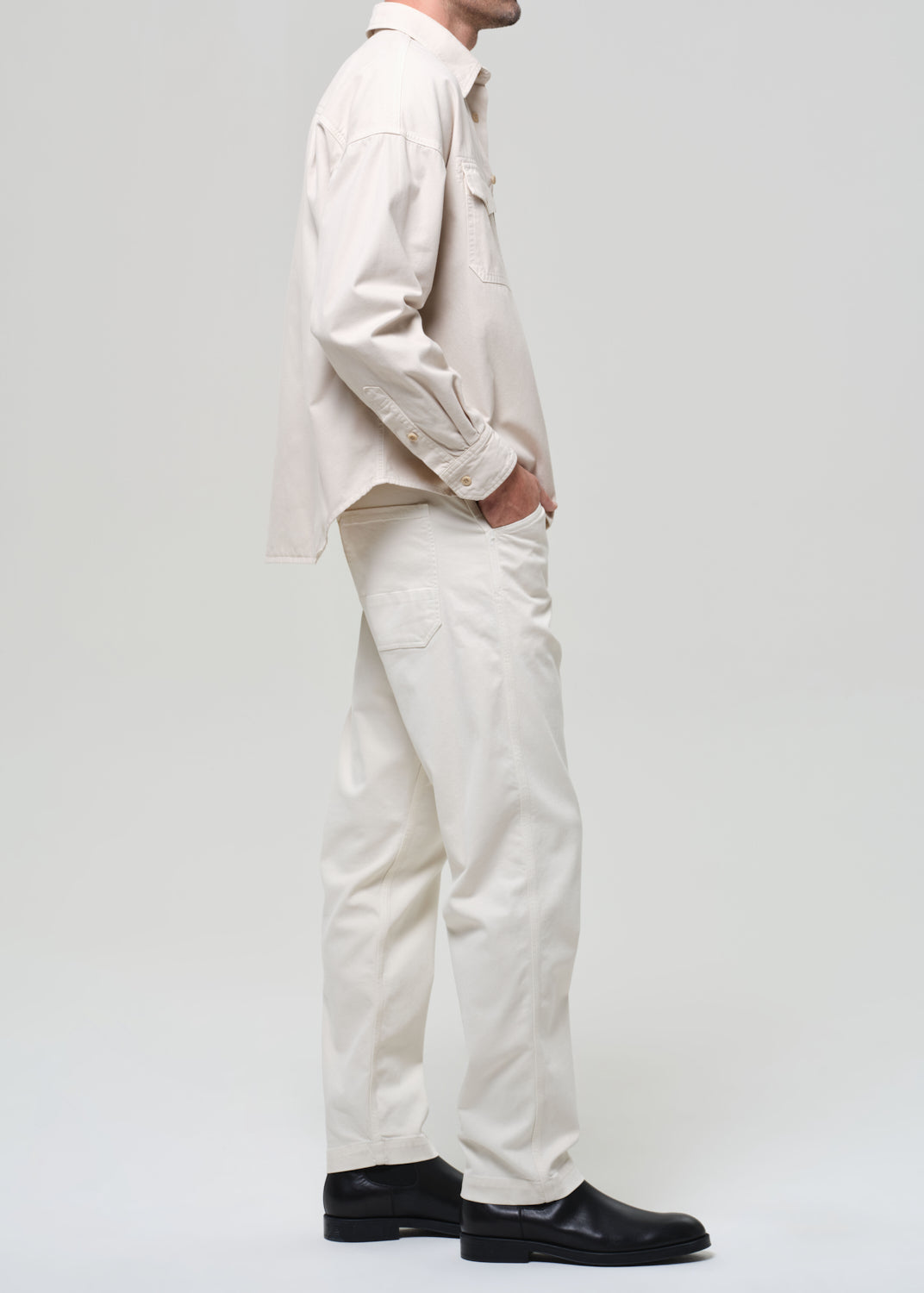 Person wearing a beige shirt and pants with black shoes on a grey background