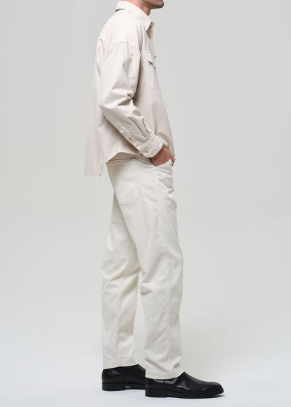 Person wearing a beige shirt and pants with black shoes on a grey background