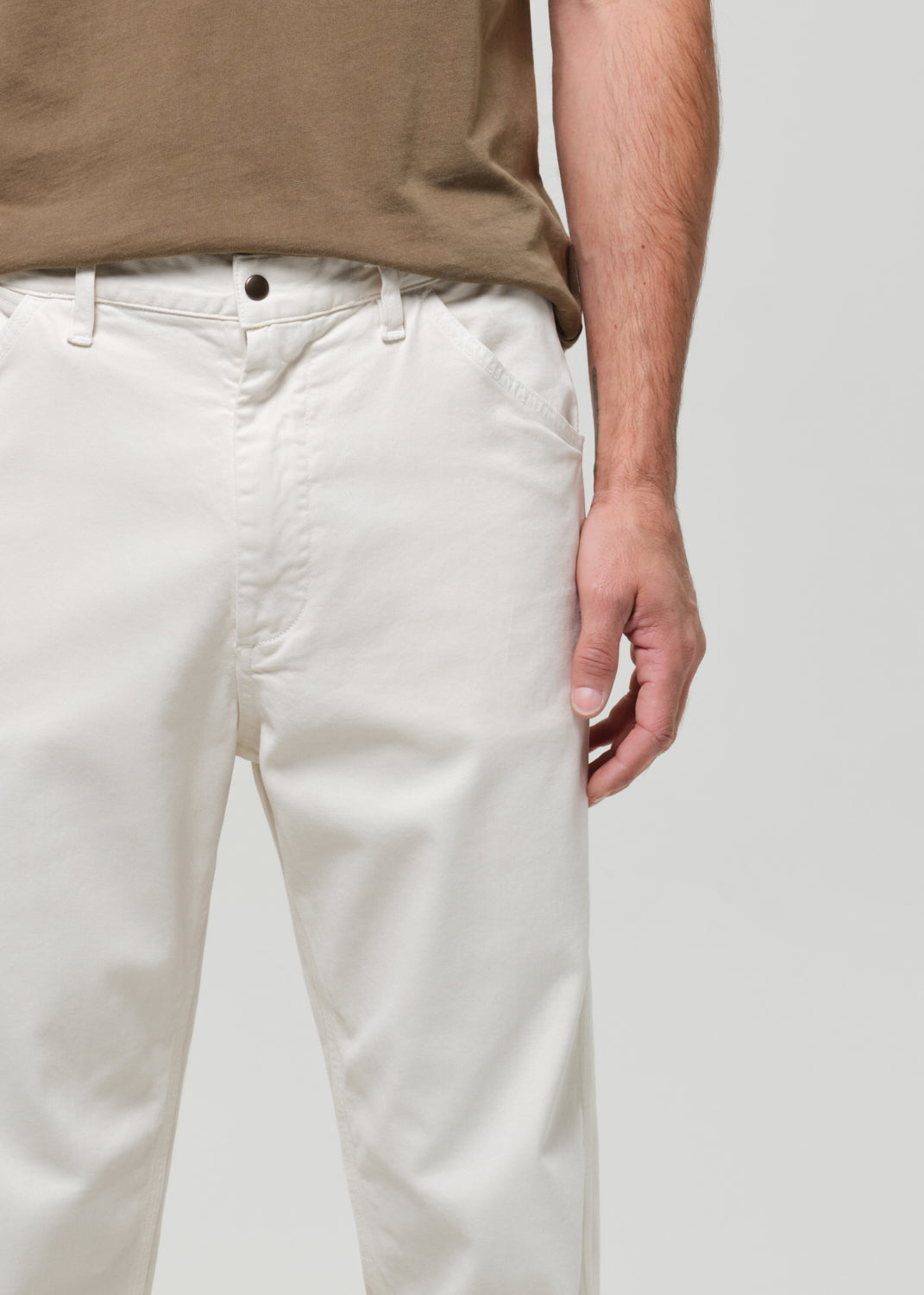 Person wearing beige shirt and white pants on a plain background