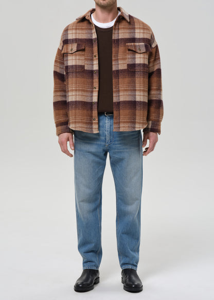 Person wearing light blue straight leg jeans with a brown plaid overshirt on a grey background.