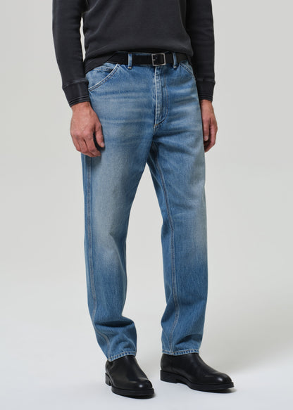 Person wearing a dark long-sleeve shirt, blue jeans, and black shoes on a grey background