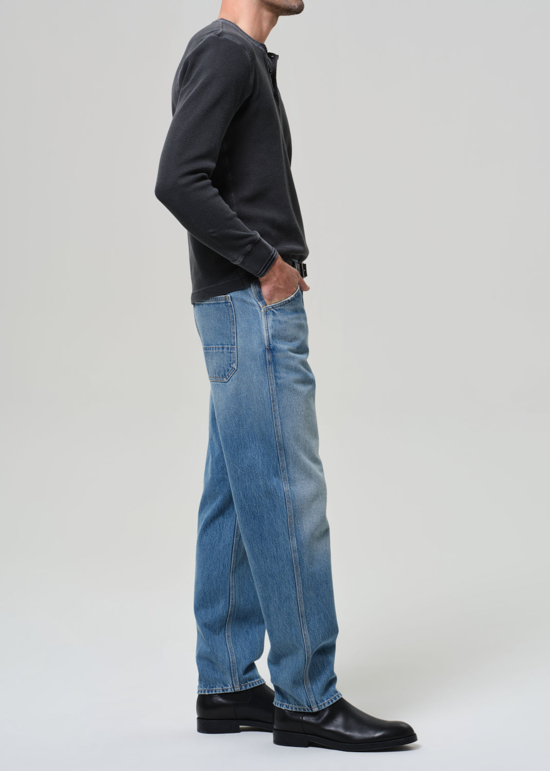Person wearing a dark long-sleeve shirt, blue jeans, and black shoes on a grey background