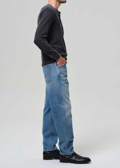 Person wearing a dark long-sleeve shirt, blue jeans, and black shoes on a grey background