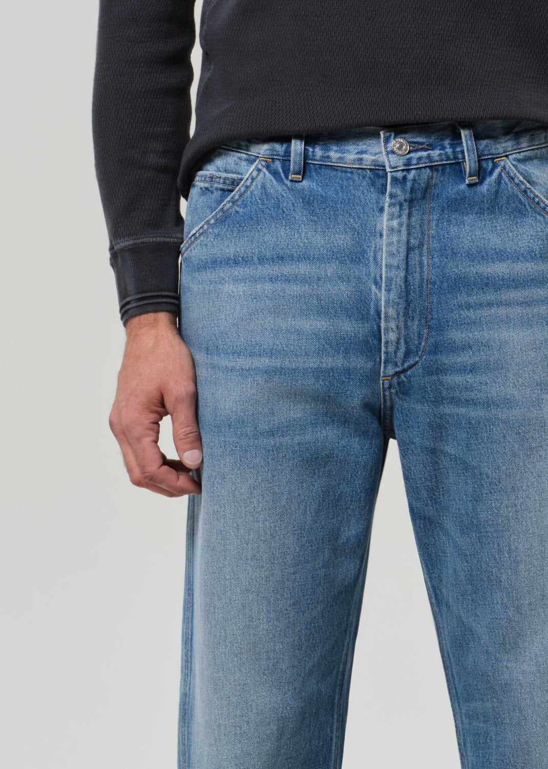 Person wearing a dark long-sleeve shirt, blue jeans, and black shoes on a grey background