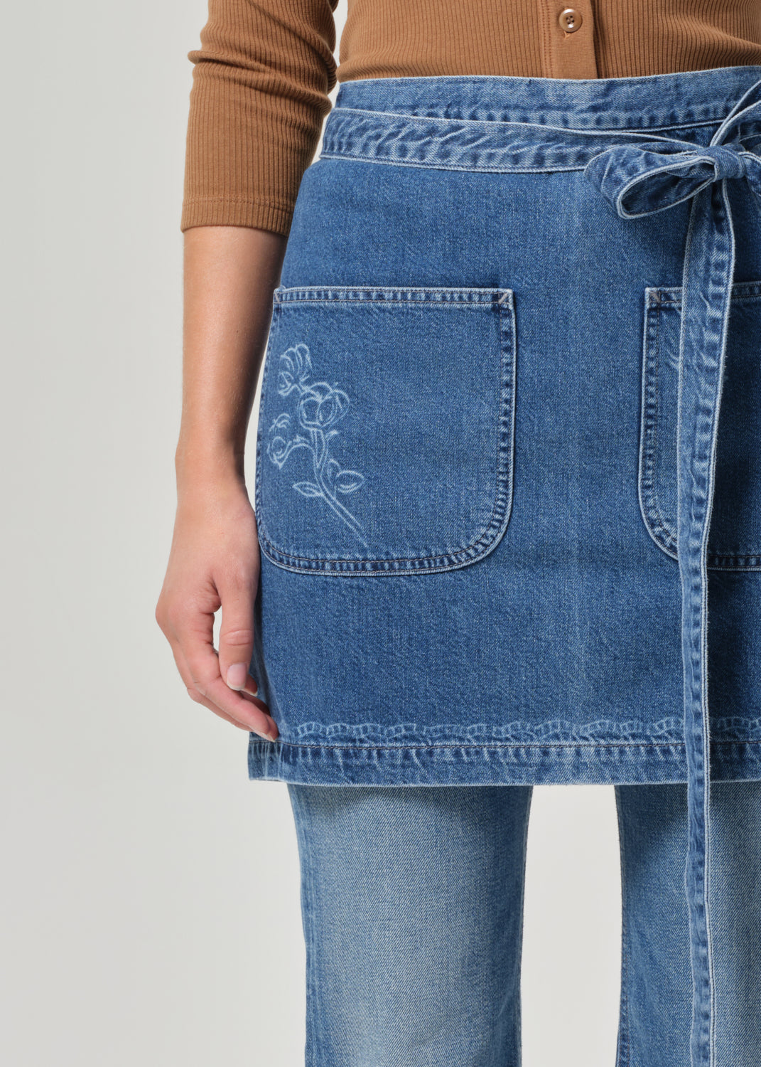 Person wearing a blue denim apron with floral embroidery on a plain background