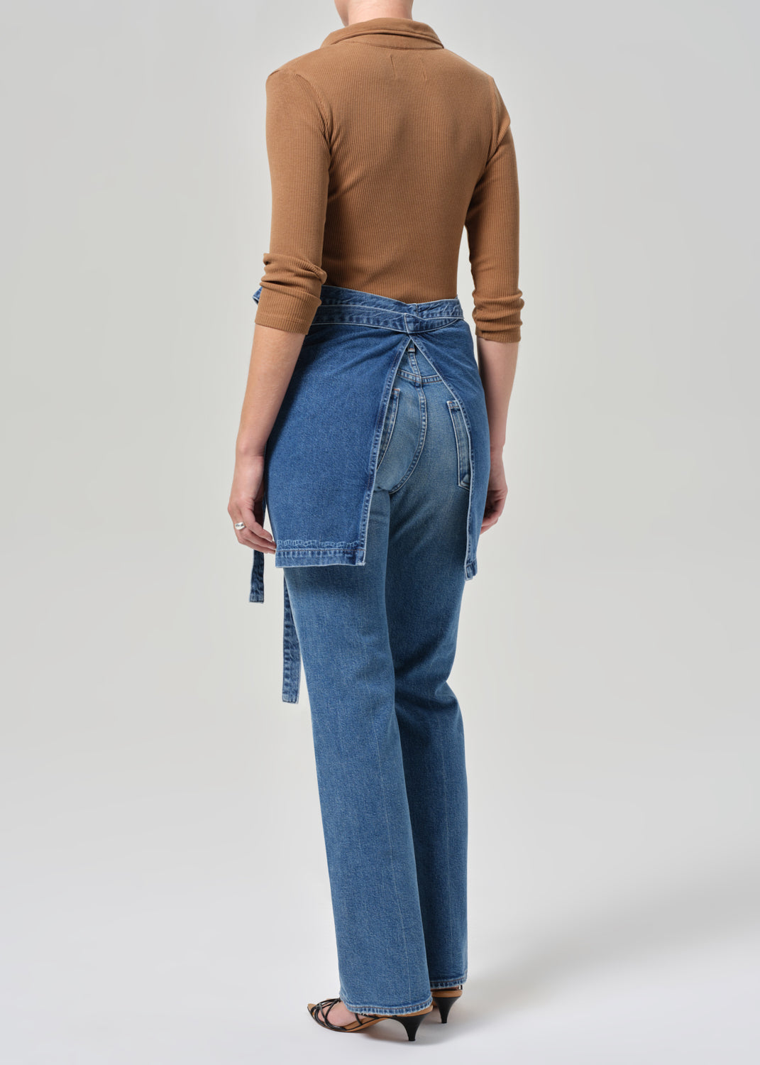 Person wearing a brown top and blue apron and jeans with a white background