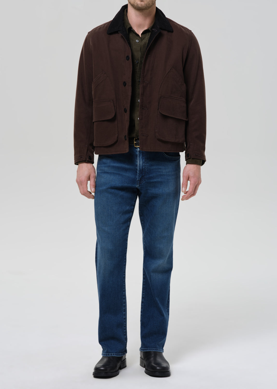 Man wearing a brown jacket and blue jeans on a grey background