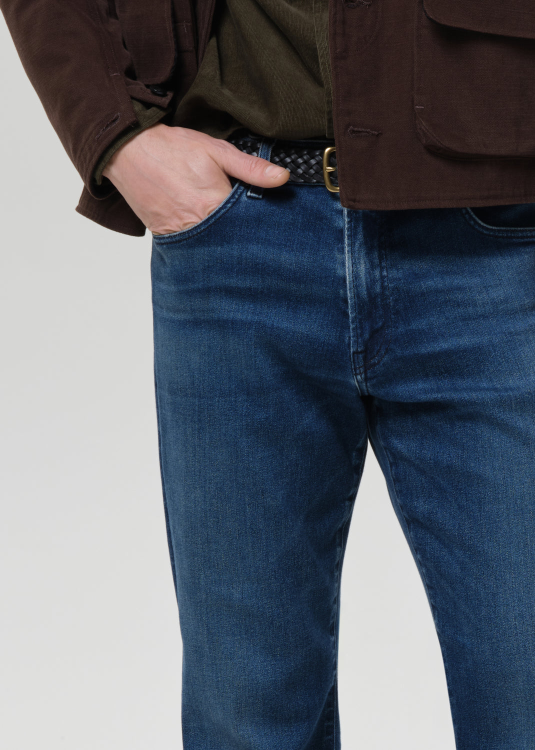 Person wearing blue jeans and a brown jacket on a grey background