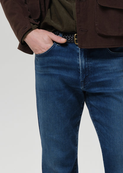 Person wearing blue jeans and a brown jacket on a grey background