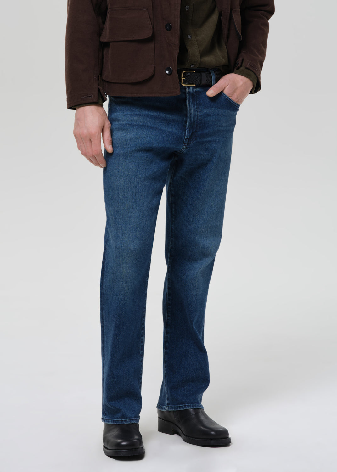 Person wearing blue jeans and a brown jacket on a grey background