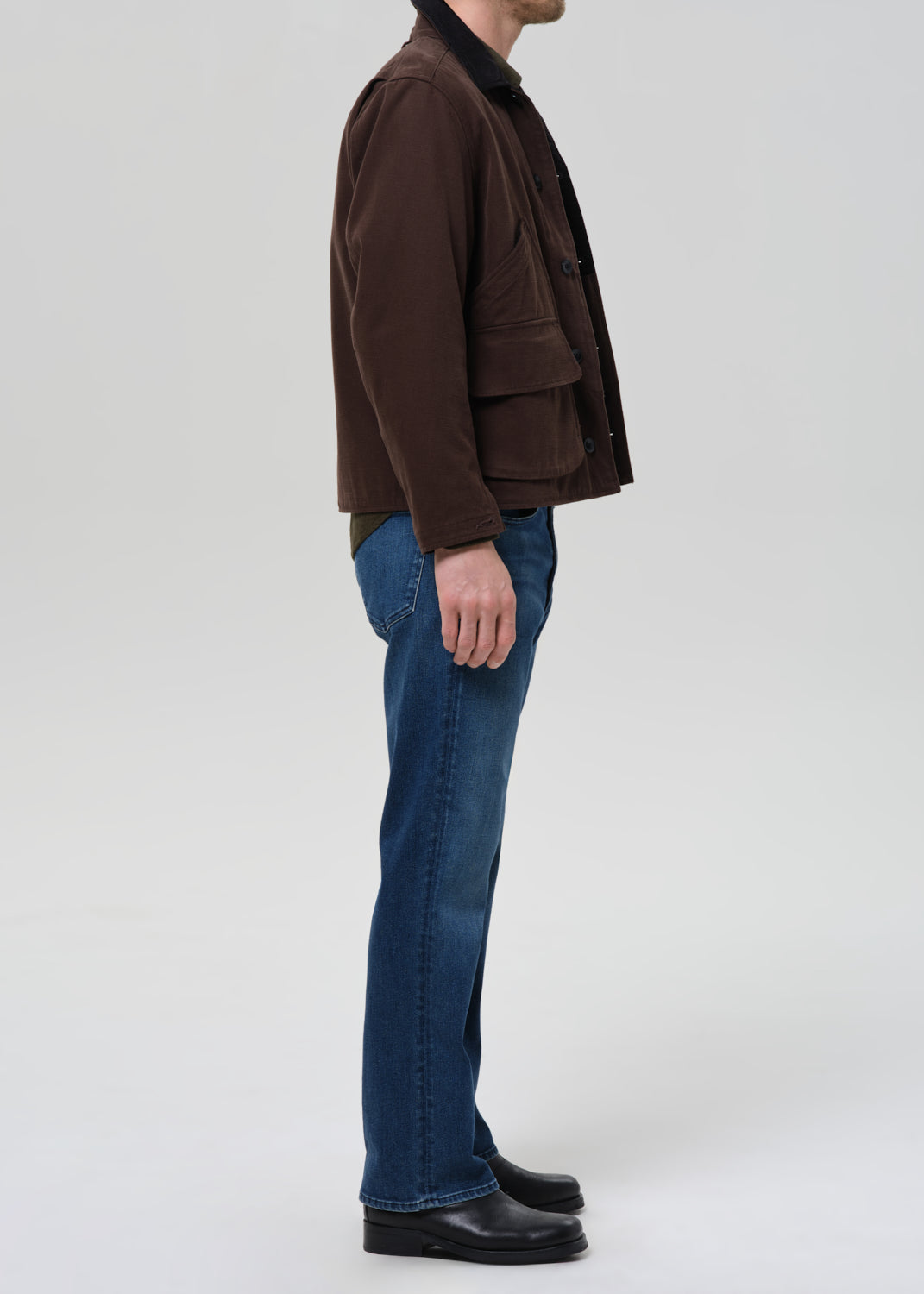 Person wearing a brown jacket and blue jeans on a grey background