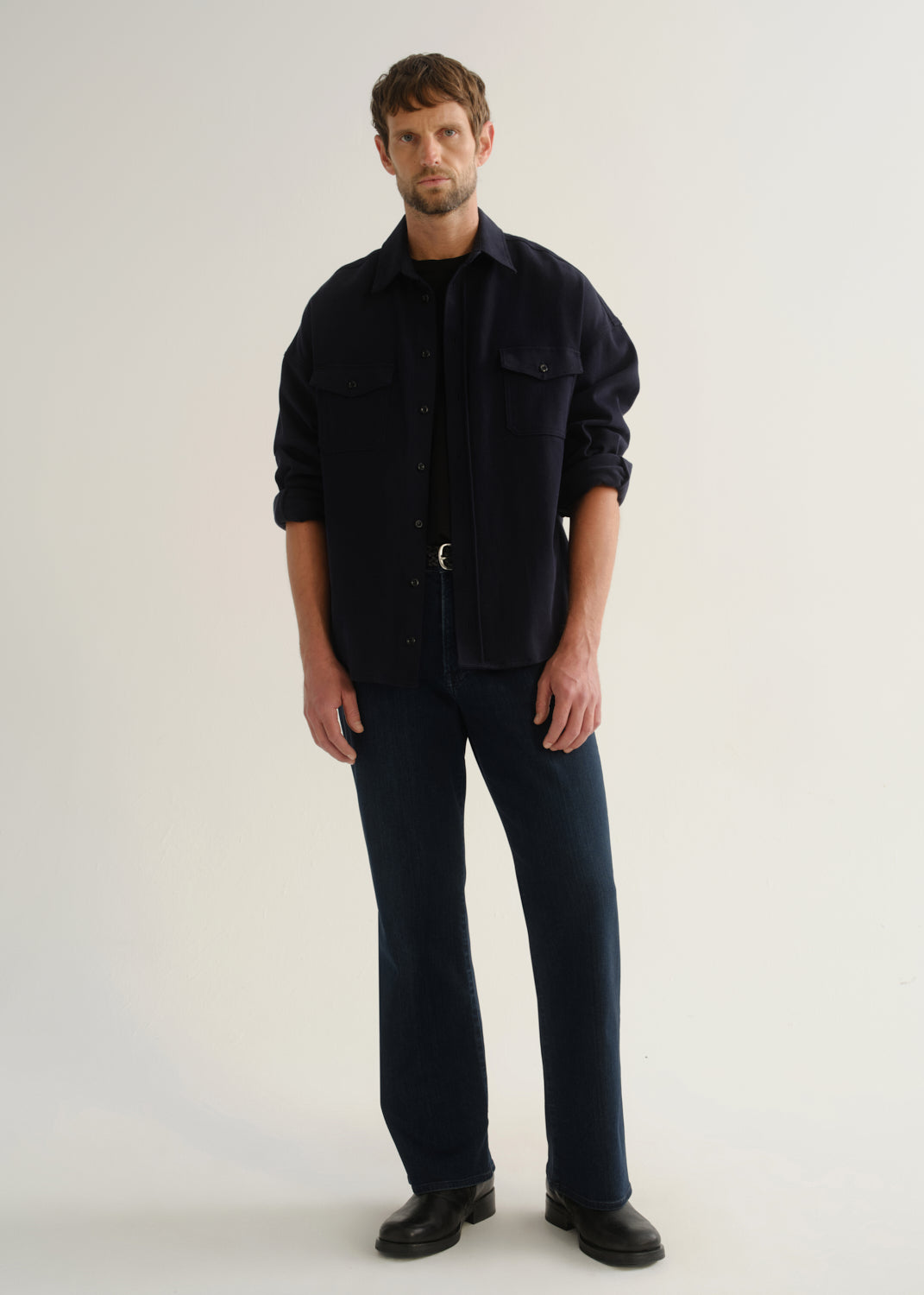 Person wearing dark indigo wide leg jeans with a navy long sleeve shirt and black boots, front full body view on a light grey background.