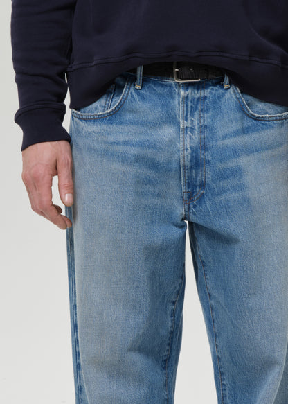 Person wearing blue jeans and a dark shirt on a grey background