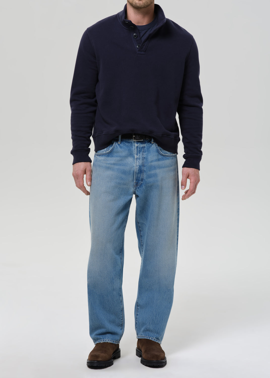 Person wearing a navy sweater and light blue jeans on a grey background