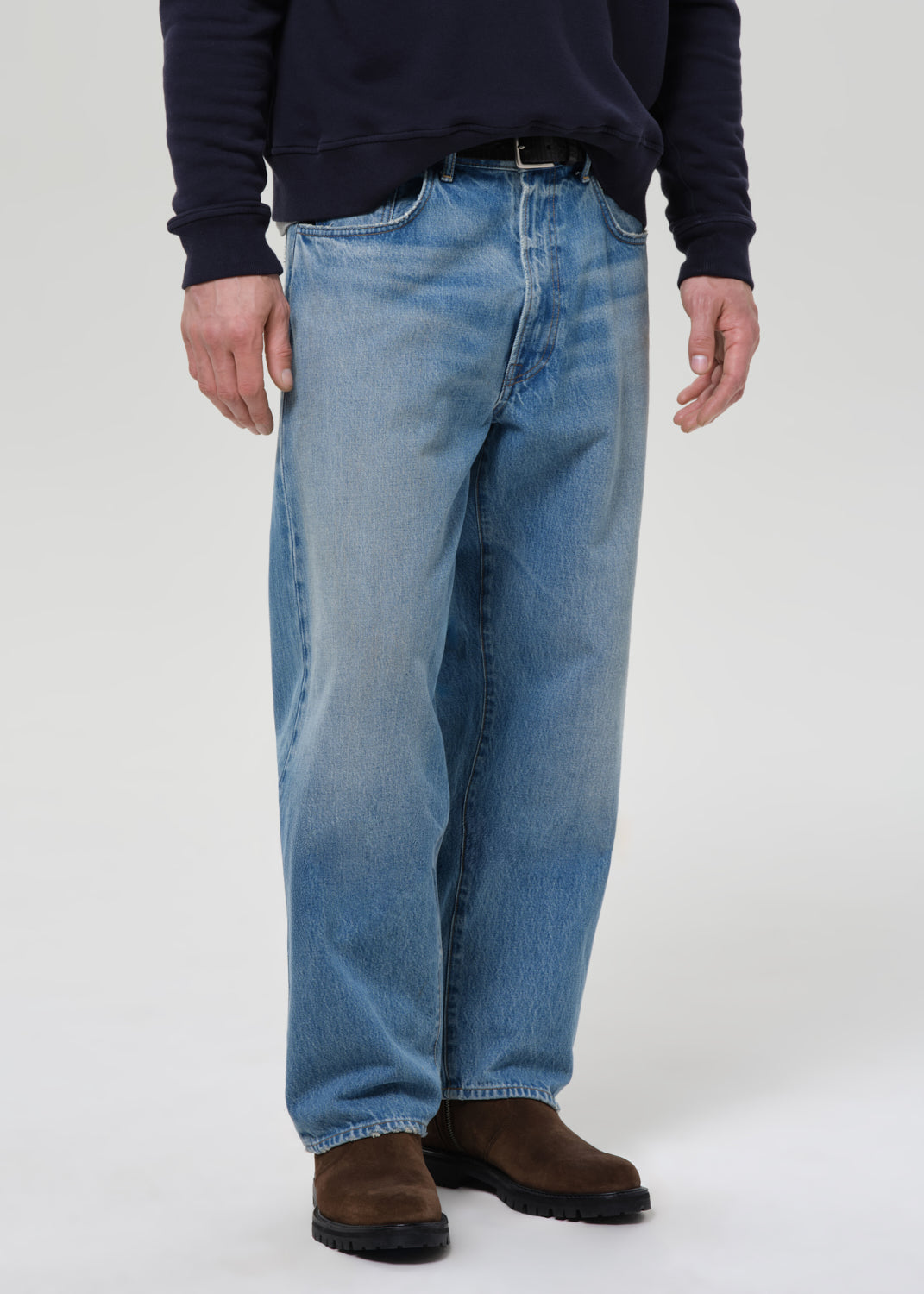 Person wearing blue jeans and a dark sweater on a grey background