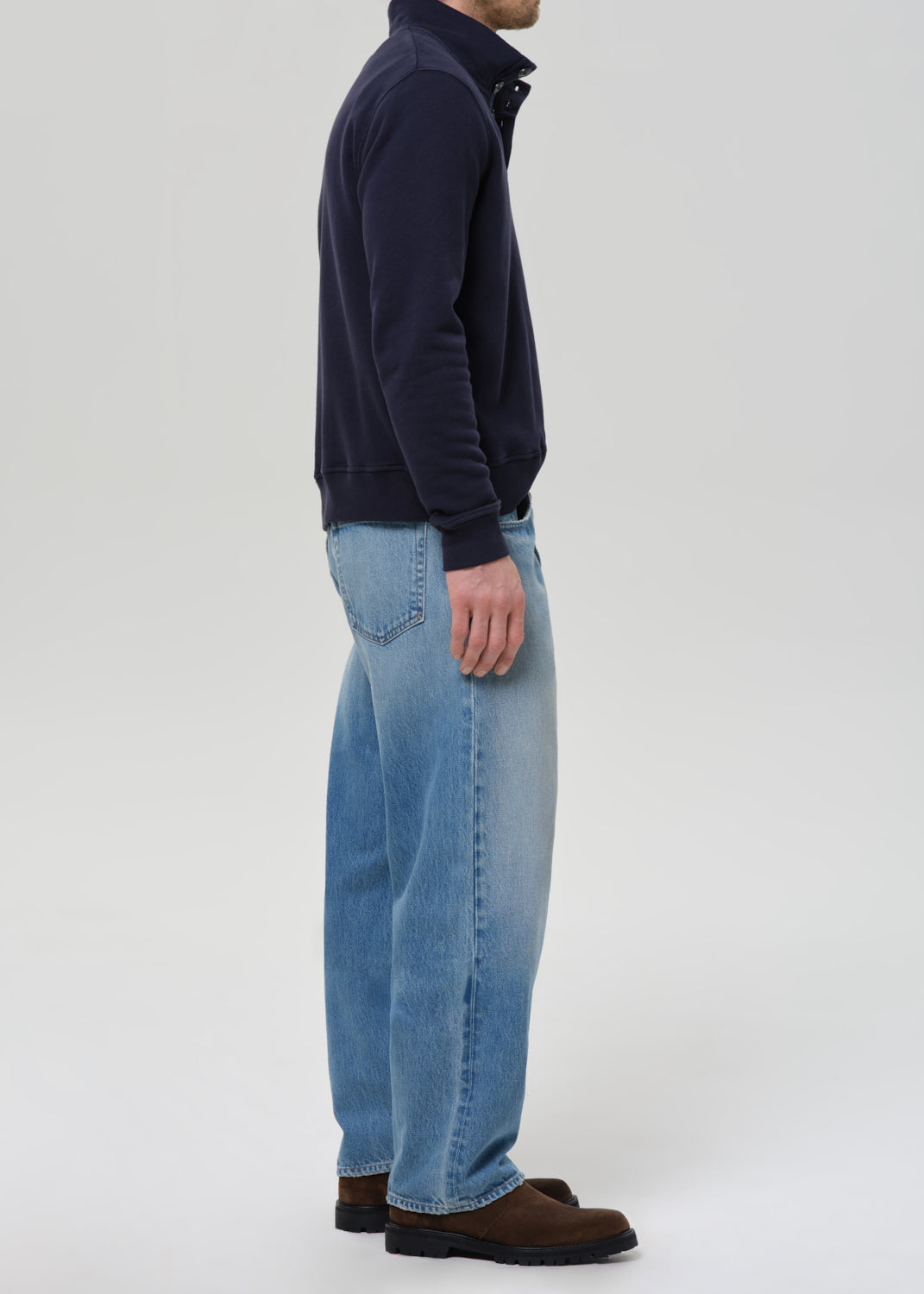 Person wearing a navy sweater and blue jeans on a grey background