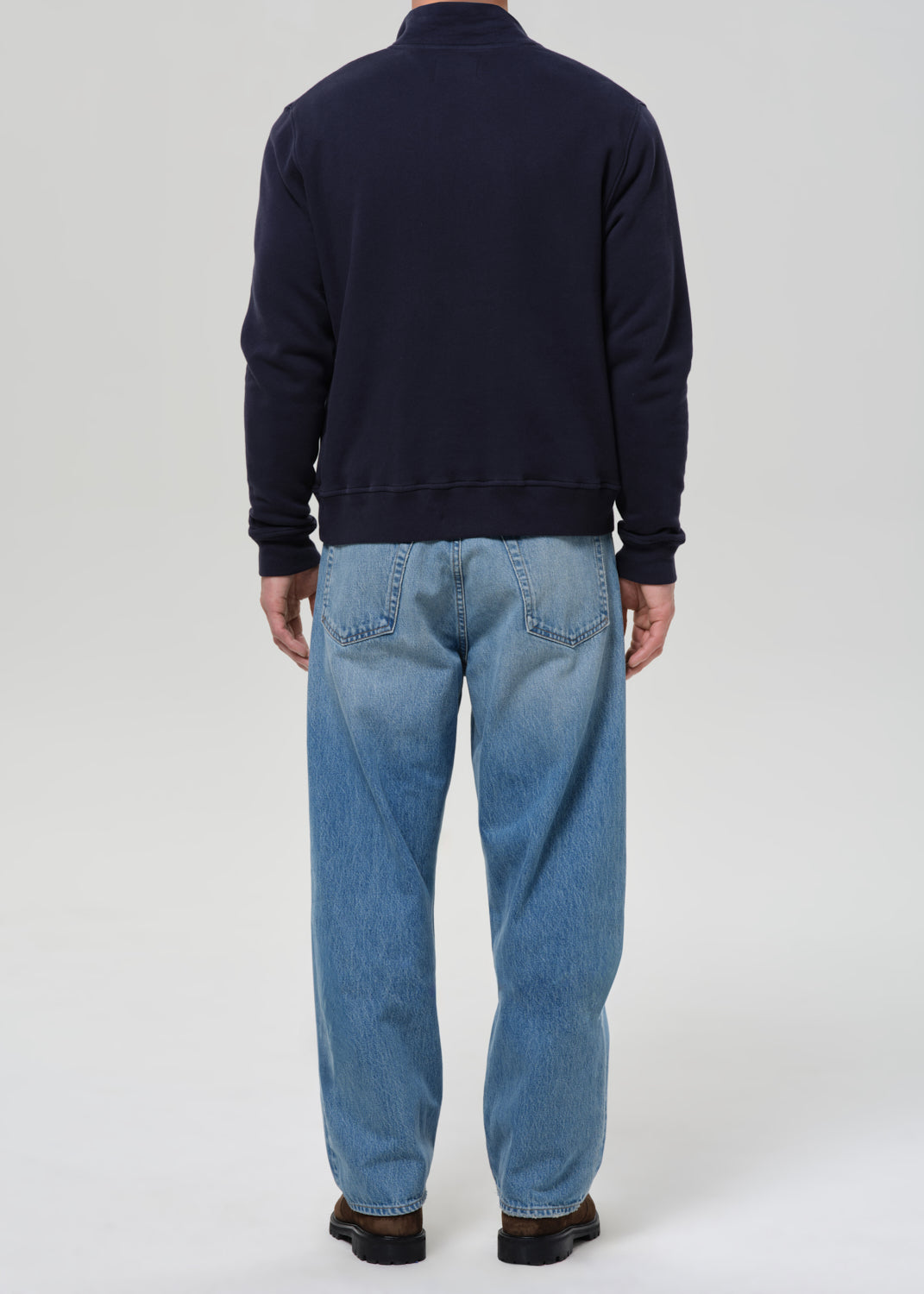 Person wearing a navy sweater and blue jeans on a grey background