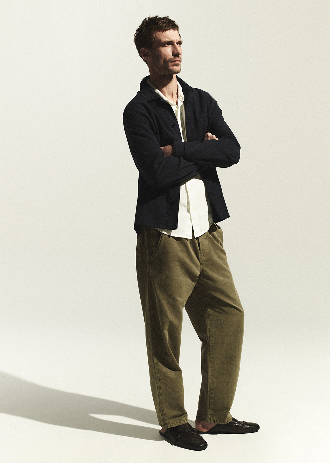 Man wearing a navy shirt and green pants standing against a white background