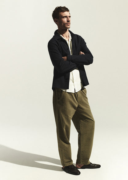 Man wearing a navy shirt and green pants standing against a white background
