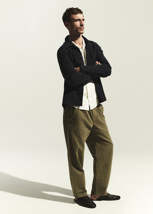 Man wearing a navy shirt and green pants standing against a white background