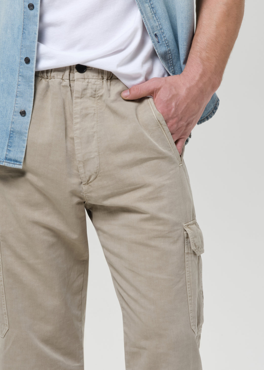 Person wearing beige cargo pants with a light blue denim jacket on a plain background
