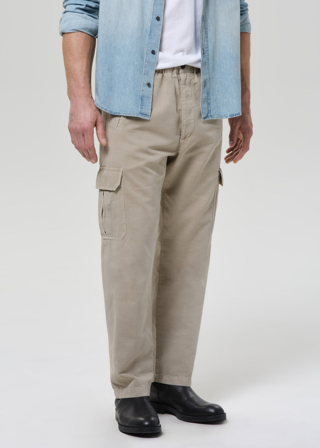 Person wearing beige cargo pants with a denim shirt on a plain background