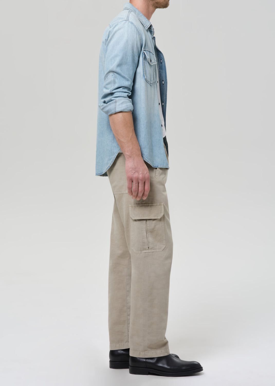 Person wearing a light blue denim shirt and beige pants on a plain background