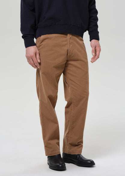Person wearing brown pants and black shoes on a grey background.
