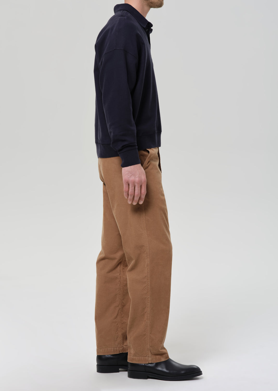 Man wearing a navy sweater and brown pants on a grey background.
