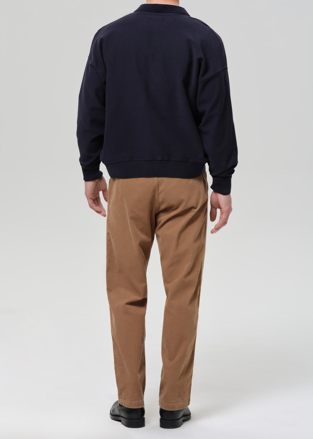 Person wearing a navy sweater and brown pants on a grey background.