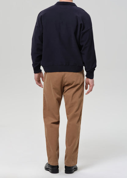Person wearing a navy sweater and brown pants on a grey background.